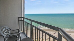 Un balcone con vista sulla spiaggia, una sedia e una ringhiera.