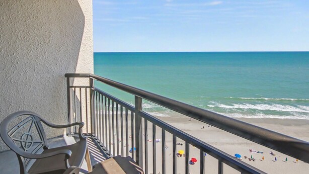 A balcony with a view of the beach, a chair, and a railing. - Oceanfront Studio w/ Two Queens + Beach & Pools (Myrtle Beach)