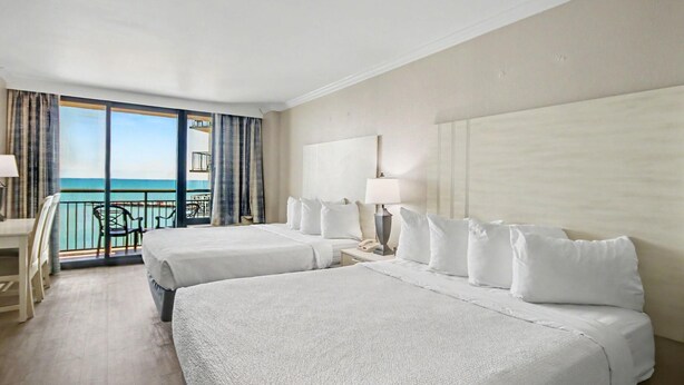 A hotel room with two beds, a balcony with a view of the sea, a desk, and a chair. - Oceanfront Studio w/ Two Queens + Beach & Pools (Myrtle Beach)