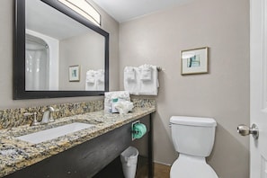 A bathroom with a granite countertop, a sink, a mirror, a toilet, and a trash can. - Oceanfront Studio w/ Two Queens + Beach & Pools (Myrtle Beach)