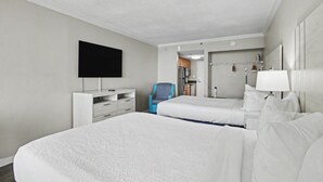 Hotellihuone, jossa on kaksi sänkyä, televisio, työpöytä, tuoli sekä kylpyhuone, jossa on peili ja pesuallas.