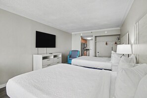 A hotel room with two beds, a TV, a desk, a chair, and a bathroom with a mirror and sink. - Oceanfront Studio w/ Two Queens + Beach & Pools (Myrtle Beach)