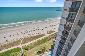 Ein Hochhaus-Hotel mit Blick auf einen Strand, mit Reihen von Sonnenschirmen und Liegestühlen.