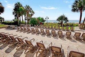 A beachside lounge area with rows of sun loungers and tables, palm trees, and a view of the ocean. - Oceanfront Studio w/ Two Queens + Beach & Pools (Myrtle Beach)