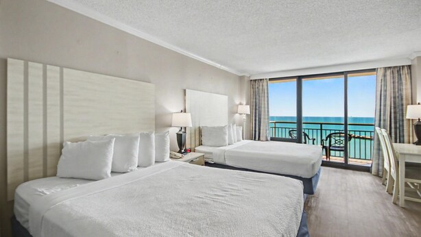 A hotel room with two beds, a desk, and a balcony with a view of the sea. - Oceanfront Studio w/ Two Queens + Beach & Pools (Myrtle Beach)