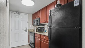 A kitchen with wooden cabinets, a black refrigerator, a microwave, and a stove. - Oceanfront Studio w/ Two Queens + Beach & Pools (Myrtle Beach)