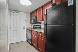 A kitchen with wooden cabinets, a black refrigerator, a microwave, and a stove. - Oceanfront Studio w/ Two Queens + Beach & Pools (Myrtle Beach)