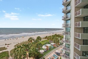 Een hoog hotel met balkons met uitzicht op een strand, een zwembad en uitzicht op de oceaan.