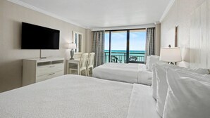 A hotel room with two beds, a desk, a chair, a TV, and a balcony with a view of the ocean. - Oceanfront Studio w/ Two Queens + Beach & Pools (Myrtle Beach)