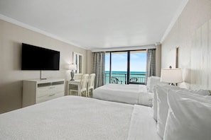 A hotel room with two beds, a desk, a chair, a TV, and a balcony with a view of the ocean. - Oceanfront 7th Floor Studio w/ Balcony & Kitchenette | Dog Friendly (Myrtle Beach)