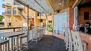 An outdoor pool bar area with tables and chairs, a menu board, and a view of a building with balconies. - Ocean View King Room + Beach Access + Lazy River (Myrtle Beach)