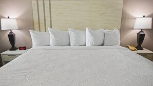 Una cama con una colcha blanca texturizada, un cabecero con diseño de rayas verticales, dos lámparas de noche, un reloj digital y un teléfono en la mesita de noche.