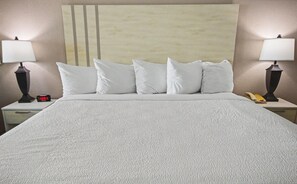 Una cama con una colcha blanca texturizada, un cabecero con diseño de rayas verticales, dos lámparas de noche, un reloj digital y un teléfono en la mesita de noche.