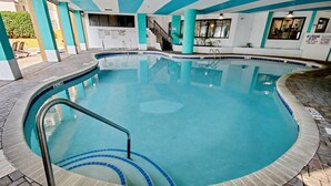 Una piscina interior con borde de azulejos, una escalera metálica y una escalera que lleva a un nivel superior.