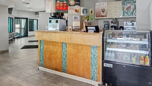 Interno di un caffè con un bancone, cartelli con il menù, un frigorifero pieno di bevande e un'area salotto con vista.