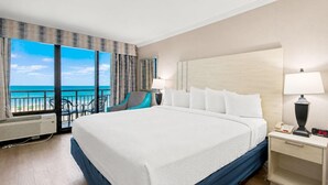 Camera d'albergo con un letto grande, una scrivania con lampada, una sedia e vista sull'oceano.