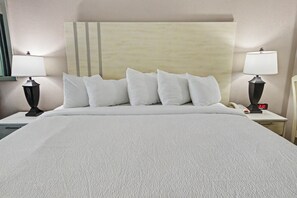 A hotel room with a large bed, two bedside tables with lamps, a clock, and a headboard with vertical stripes. - Ocean View King Room + Beach Access + Lazy River (Myrtle Beach)