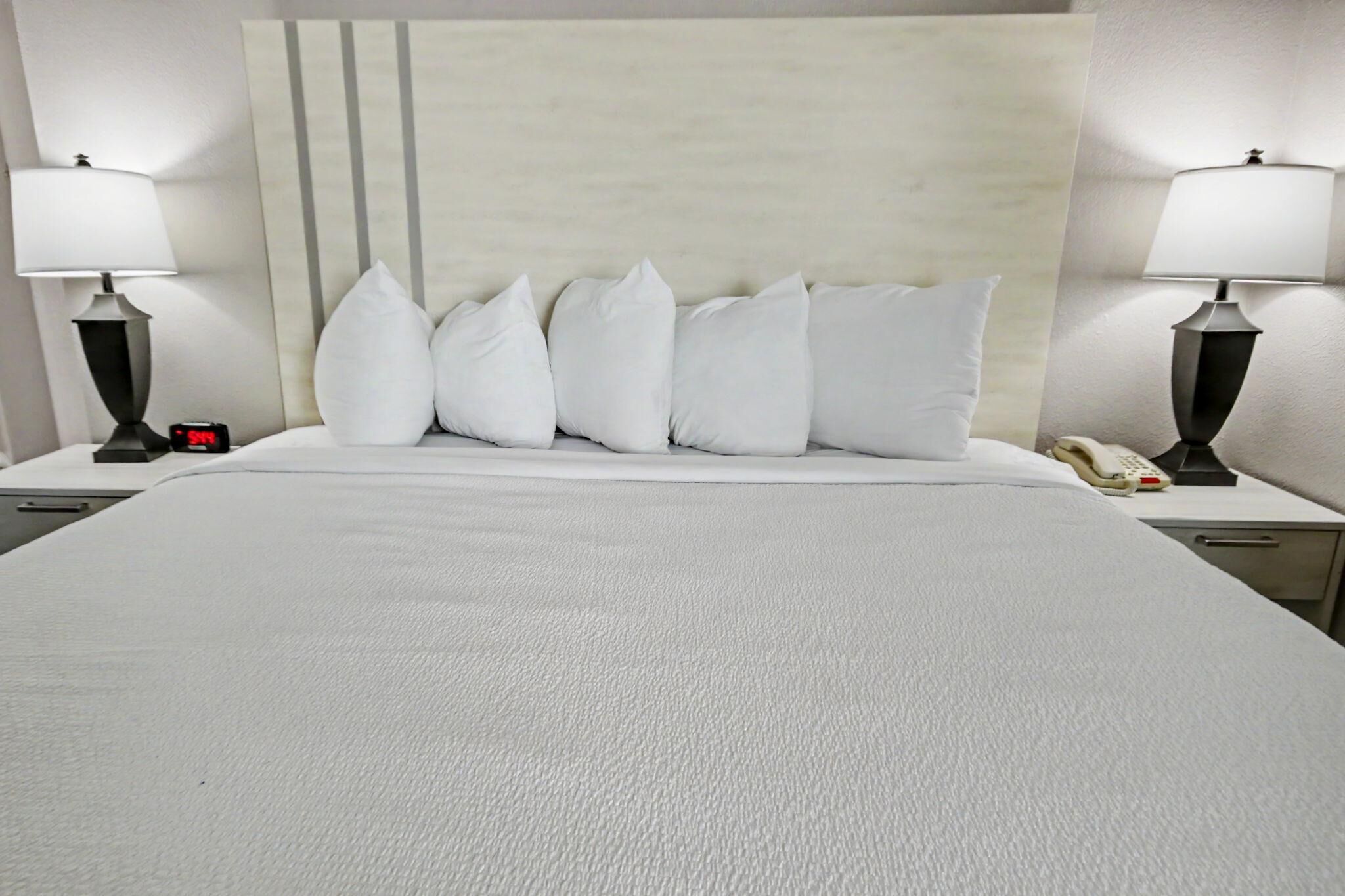 Ein Hotelzimmer mit einem großen Bett, zwei Nachttischen, einem Beistelltischchen mit Lampe, einem Telefon und einer digitalen Uhr.