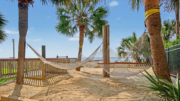 Ett sandigt strandområde med hängmattor och träkonstruktioner.