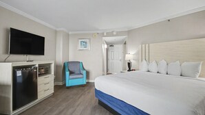 Ett hotellrum med en säng, en tv, ett minikylskåp, en stol och en dörr som leder till ett annat rum.