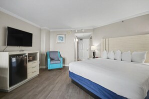 Ett hotellrum med en säng, en tv, ett minikylskåp, en stol och en dörr som leder till ett annat rum.