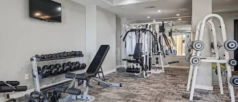 A gym with weightlifting equipment, dumbbells, and a TV on the wall.