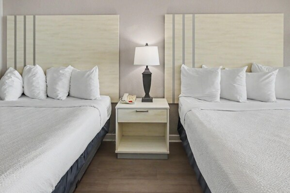 A hotel room with two beds, a nightstand with a lamp, and a telephone.