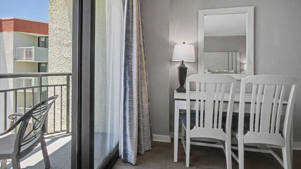 A balcony with a chair, a table, and a lamp. - Oceanfront Studio w/ Two Queens + Beach & Pools (Myrtle Beach)
