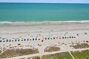 Une plage bordée de rangées de parasols et où l’on voit des gens se prélasser.