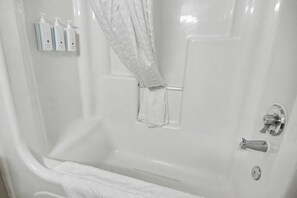 A white bathtub with a shower curtain, a towel, and three bottles of toiletries. - Oceanfront Studio w/ Two Queens + Beach & Pools (Myrtle Beach)