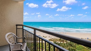 A balcony with a view of the ocean and beach, a chair, and a railing. - Oceanfront Studio w/ Two Queens + Beach & Pools (Myrtle Beach)