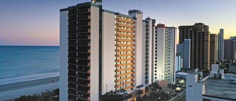A high-rise hotel with multiple floors, a beach view, and a parking area.