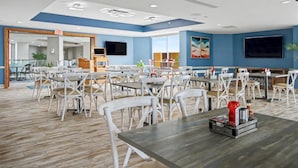 A spacious dining area with multiple tables and chairs, a flat-screen TV mounted on the wall, and a ceiling with recessed lighting. - Oceanfront Studio w/ Two Queens + Beach & Pools (Myrtle Beach)