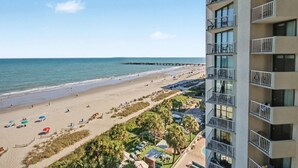 Vista de la playa desde un edificio alto, con cielo despejado, arena y un muelle que se adentra en el agua.