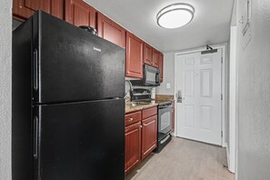 A kitchen with a black refrigerator, wooden cabinets, a microwave, and an oven. - Oceanfront Studio w/ Two Queens + Beach & Pools (Myrtle Beach)