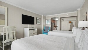 Habitación de hotel con dos camas, un escritorio, una silla, televisión y baño visible a través de una puerta abierta.