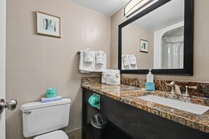A bathroom with a toilet, sink, mirror, towels, and a trash bin. - Oceanfront Studio w/ Two Queens + Beach & Pools (Myrtle Beach)