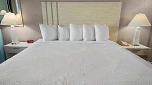 A hotel room with a large bed, two bedside lamps, a nightstand with a phone and a lamp, and a wall clock. - Ocean View King Room + Beach Access + Lazy River (Myrtle Beach)