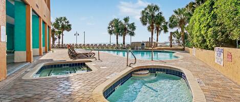 A pool area with multiple pools, lounge chairs, and palm trees.