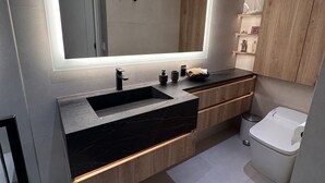 Ein modernes Badezimmer mit großem Spiegel, dunklem Marmorwaschbecken, Holzschrank und Toilette.