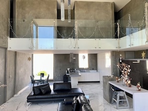 A modern interior with a black leather sofa, a kitchen area, and a glass railing.