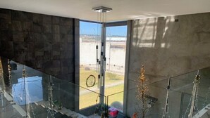 A modern interior with a glass railing, a seating area with cushions, and a view through a glass door.