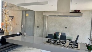 A modern kitchen with a central island, a dining area with chairs, and a large window.