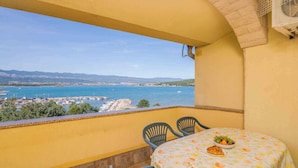 Een balkon met een tafel voor twee, met uitzicht op de kust, boten en een jachthaven.