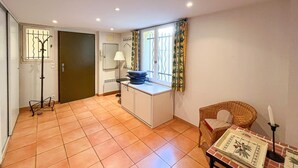 Ein Zimmer mit Fliesenboden, Schreibtisch mit Lampe, Stuhl und Fenster mit Vorhängen.