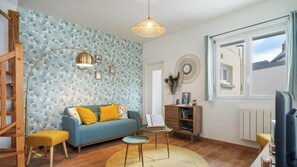 Ein Wohnzimmer mit einem blauen Sofa, einer Holzkommode, einem runden Tisch und einem großen Fenster.