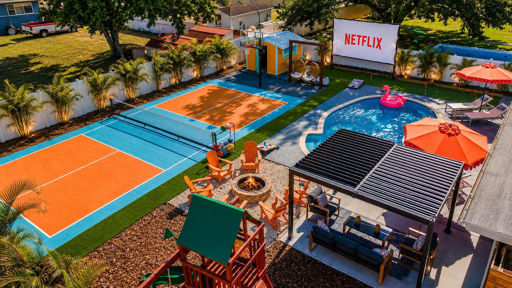 A backyard with a tennis court, a swimming pool, outdoor seating, and a large Netflix sign.