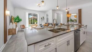 A modern kitchen with a central island, stainless steel appliances, pendant lighting, and a view to the outdoors.