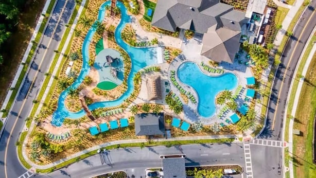 An aerial view of a resort with multiple swimming pools, a road, and surrounding greenery.