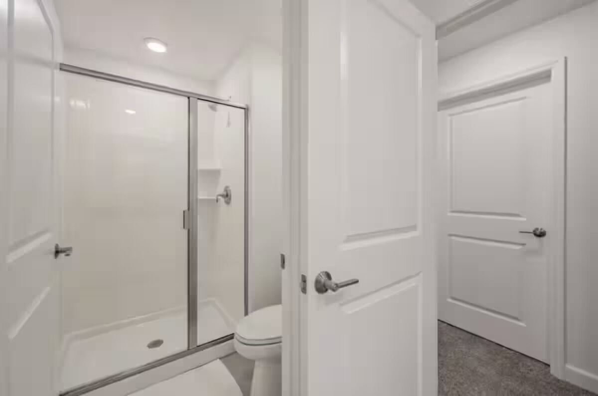 A bathroom with a glass shower enclosure, a toilet, and white doors.